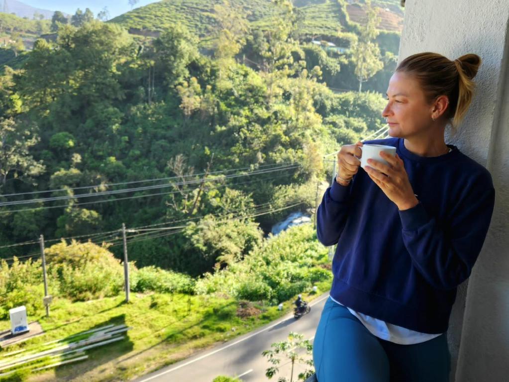 努沃勒埃利耶的住宿－Hotel Silver Falls - Nuwara Eliya，一边拿着咖啡一边望着窗外的女人