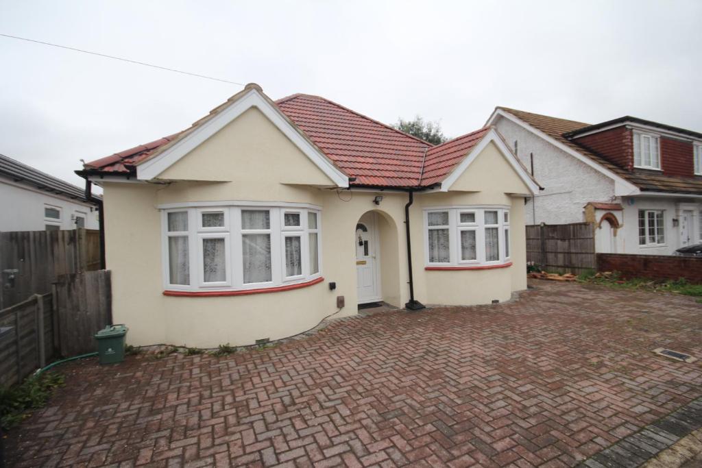 a white house with a red roof on a brick driveway at Deane House in Ruislip