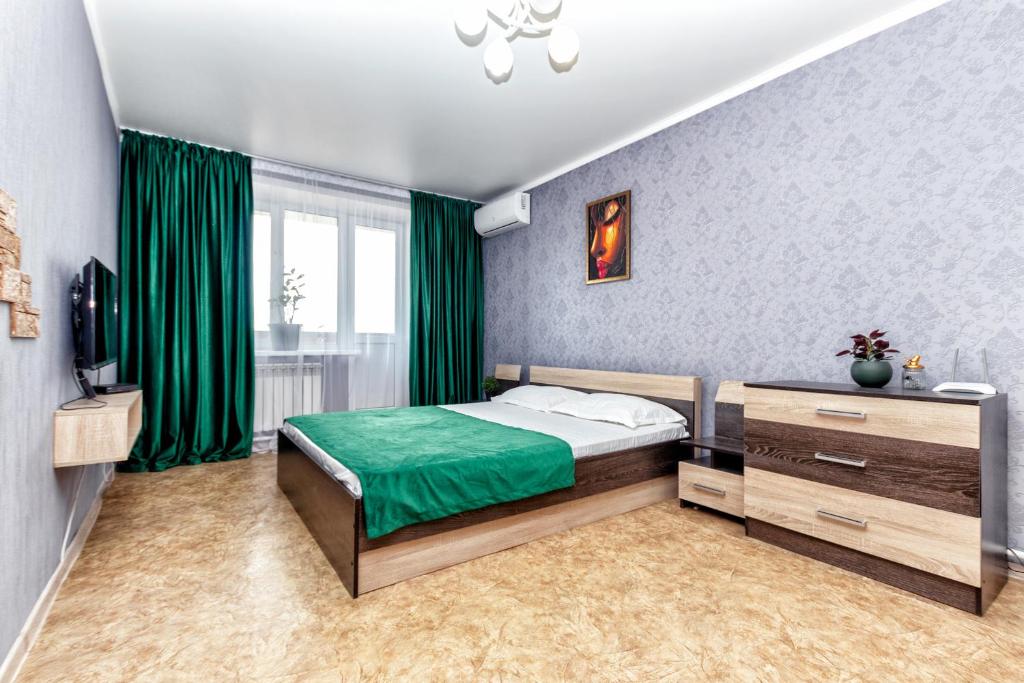 een slaapkamer met een bed met groene lakens en een televisie bij Квартира в престижном районе в новостройке in Pavlodar