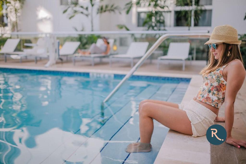 a woman in a bikini sitting next to a swimming pool at Roami at Habitat Brickell in Miami
