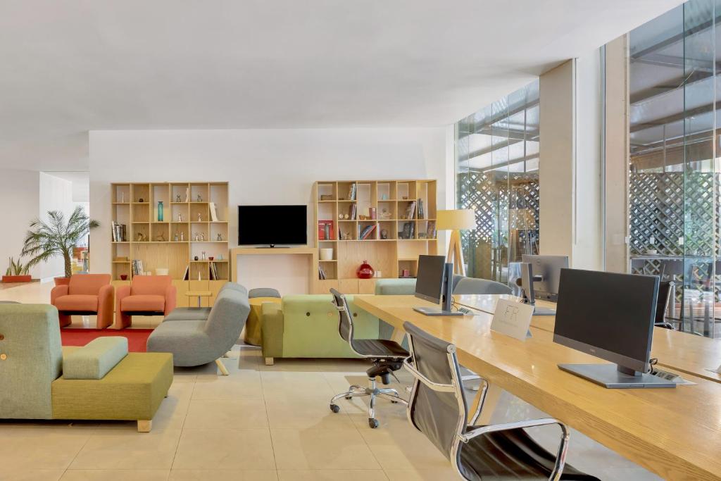 A shared hotel workspace with computer stations, desks and lounge seating.