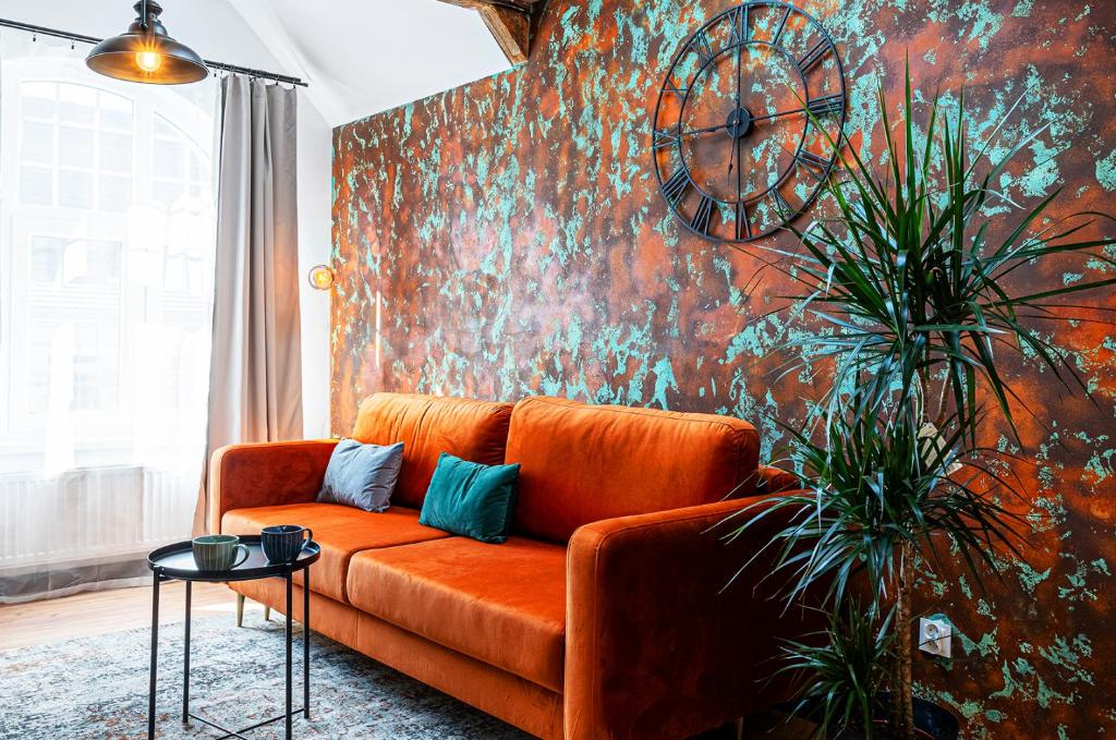 an orange couch in a living room with a clock on a wall at Apartament DWORCOWA 86 in Bydgoszcz