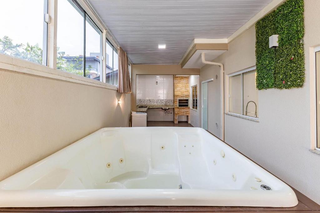 eine große weiße Badewanne in einem Zimmer mit Fenstern in der Unterkunft Casa com Jacuzzi ideal para Férias de Famílias - 3 dorms 6 pessoas in Bombinhas