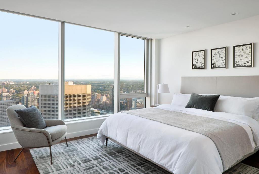 a bedroom with a bed and a chair and large windows at Award-Winning One-Bedroom Suite at Telus Sky in Calgary