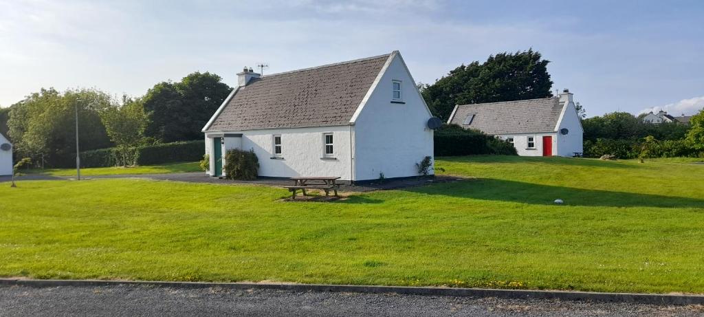 a white house with a picnic table in the grass at Traditional Cosy Cottage in Louisburgh