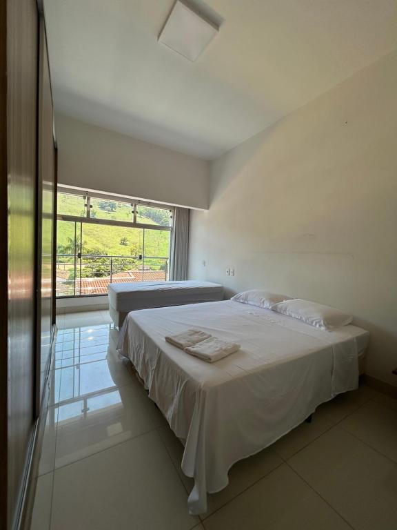 a white bedroom with a bed and a large window at Suites Silva in Capitólio