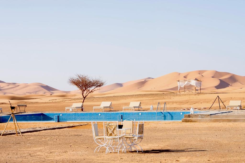 a swimming pool in the desert with sand dunes in the background at Sahara Royal Resort in Merzouga