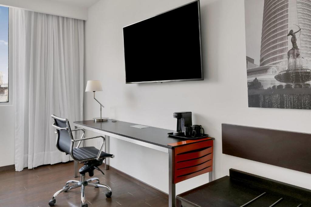 A guest-room work corner with a desk, office chair, coffee station, television, and window.