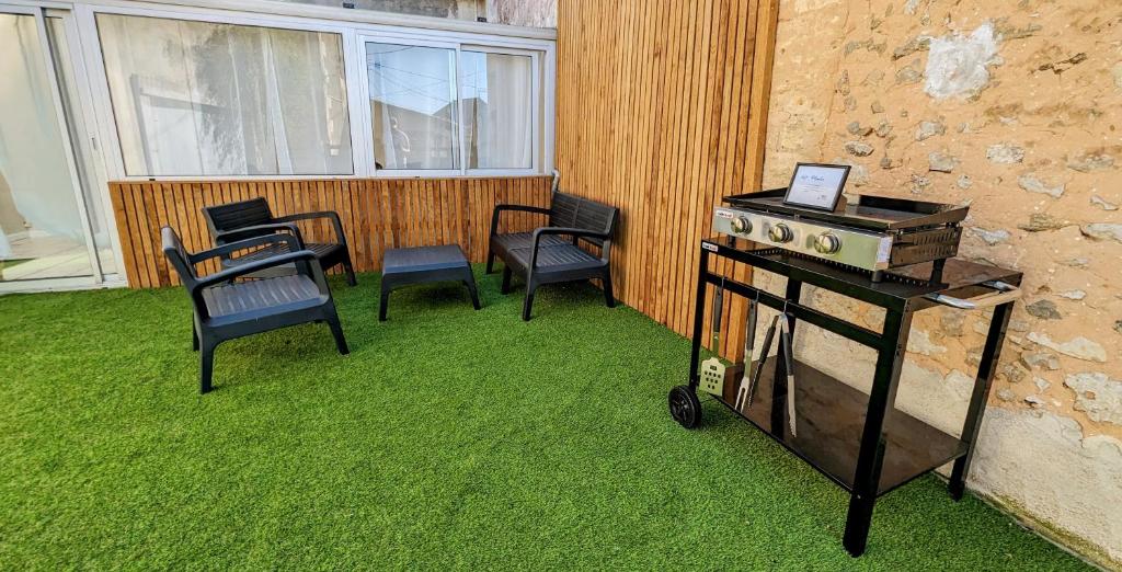 a patio with chairs and a stove on the grass at La Maison d'Elise, 3 chambres, maison de caractère in Plassac