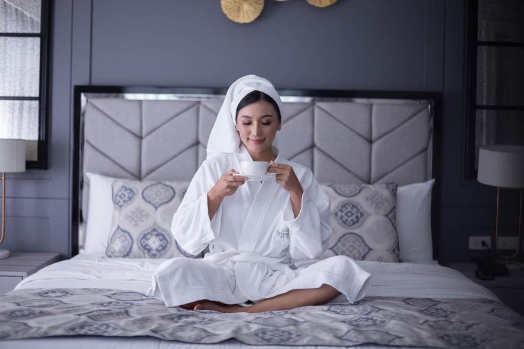 a woman in white sitting on a bed holding a cup at Stonehill Suites in Bacolod