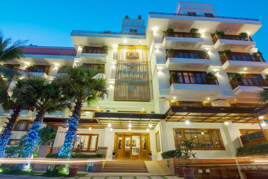 a large white building with palm trees in front of it at Cheathata CTS Hotel Siem Reap in Siem Reap