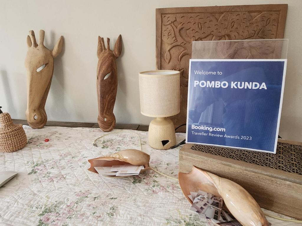 une table avec un livre, une lampe et quelques têtes d'animaux dans l'établissement POMBO KUNDA Room, à Sanyang