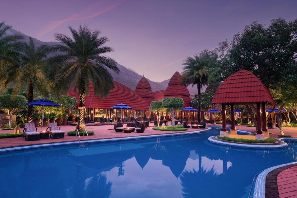 a pool at a resort with palm trees and a building at Ananta Spa & Resort, Pushkar in Pushkar