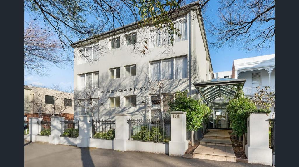 un bâtiment blanc avec une clôture devant lui dans l'établissement Knightsbridge Apartments, à Melbourne