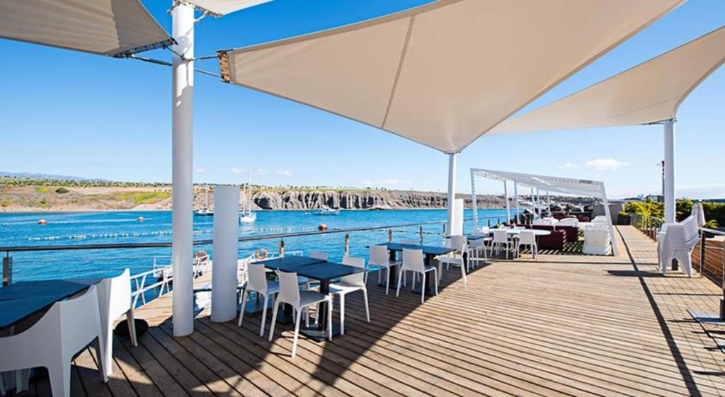a deck with tables and chairs and the water at Bungalow Pasito Blanco Marina Port 4 by VillaGranCanaria in Pasito Blanco