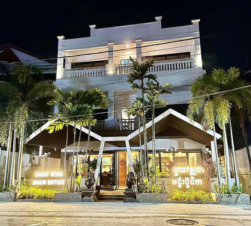 a white building with palm trees in front of it at Chhouy Vathna Angkor Boutique in Siem Reap