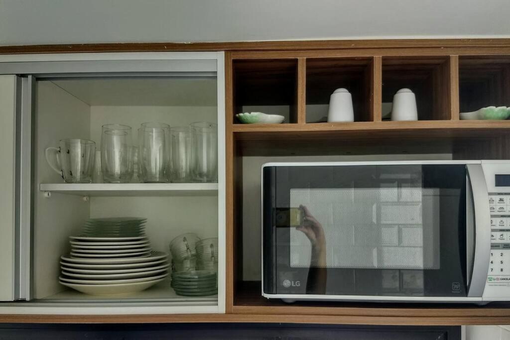 a microwave in a cabinet with plates and dishes at Ondina vista mar in Salvador