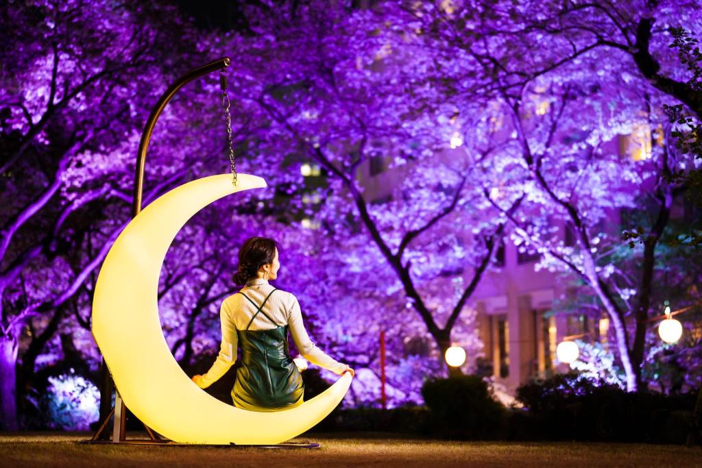 a woman sitting next to a crescent moon at night at Grand Prince Hotel Takanawa in Tokyo