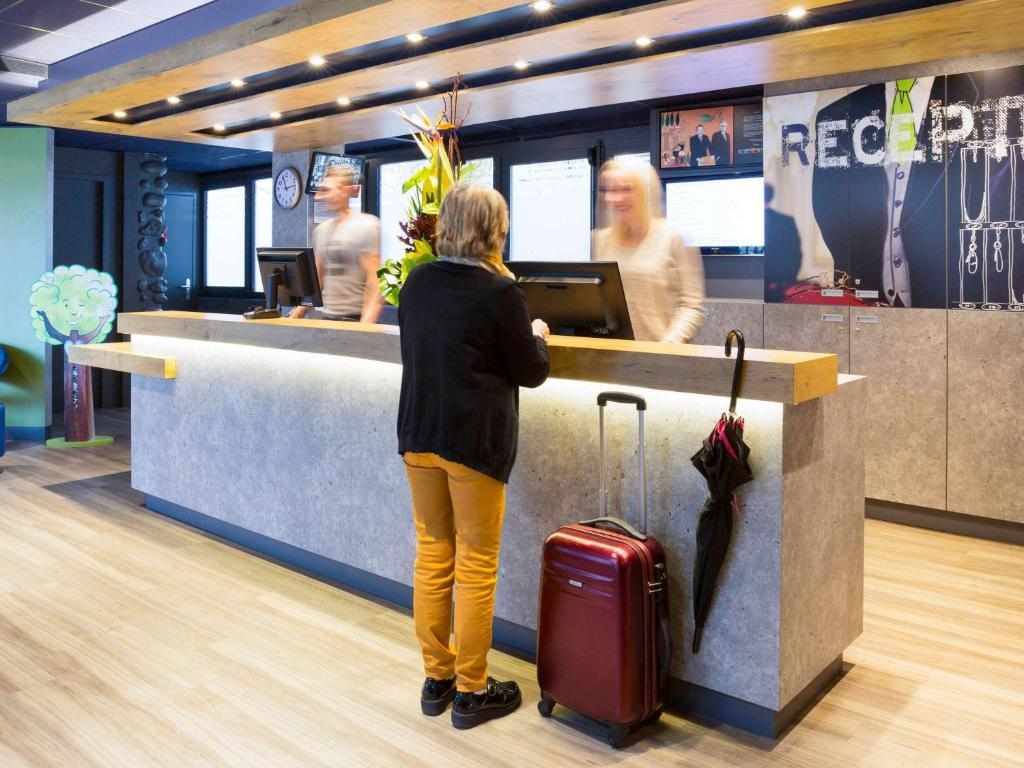 a woman standing at a counter with her luggage at ibis budget Thonon Les Bains in Thonon-les-Bains