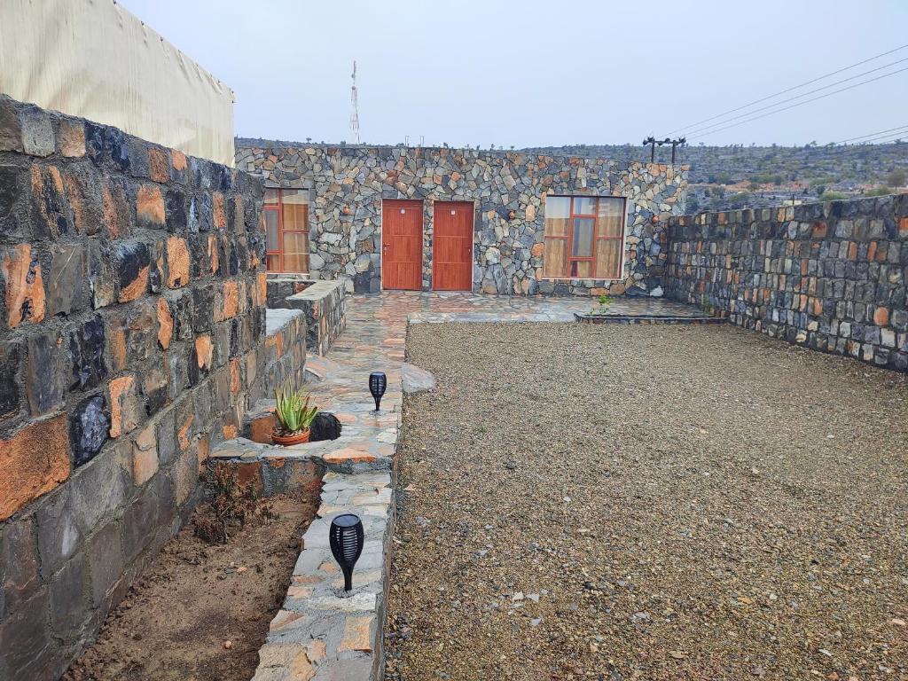 un edificio con porte rosse e un muro di pietra di Stone rest house jebel shams a Al Ḩamrāʼ