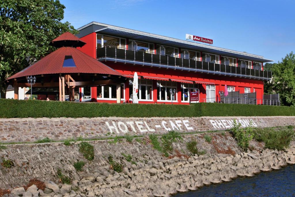 a hotel with a red building next to a river at Hotel Rheinkönig in Kamp-Bornhofen