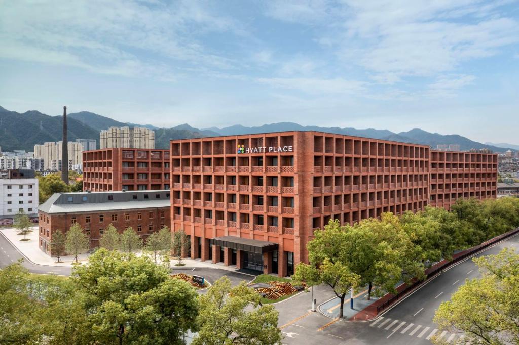 un grande edificio in mattoni rossi con montagne sullo sfondo di Hyatt Place Jingdezhen Taoxichuan a Jingdezhen