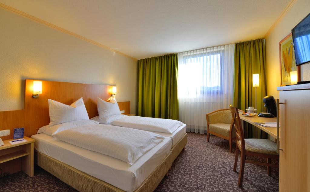 レーオンベルクにあるPLAZA INN Leonbergの大きなベッドとデスクが備わるホテルルームです。