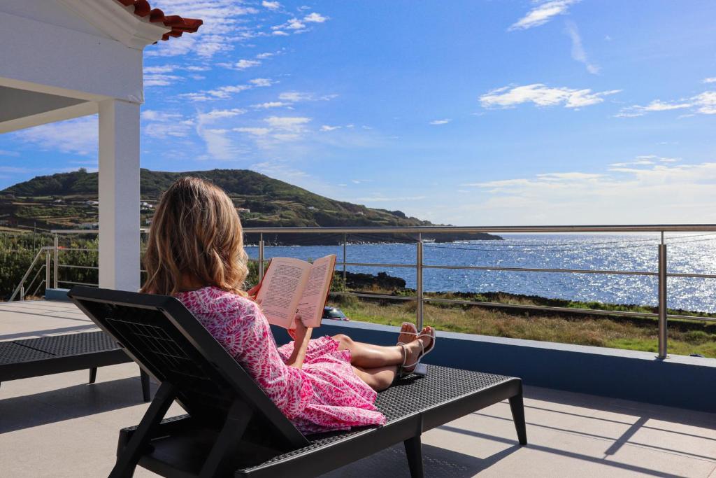a woman sitting in a chair reading a book at Villas da Salga in Angra do Heroísmo