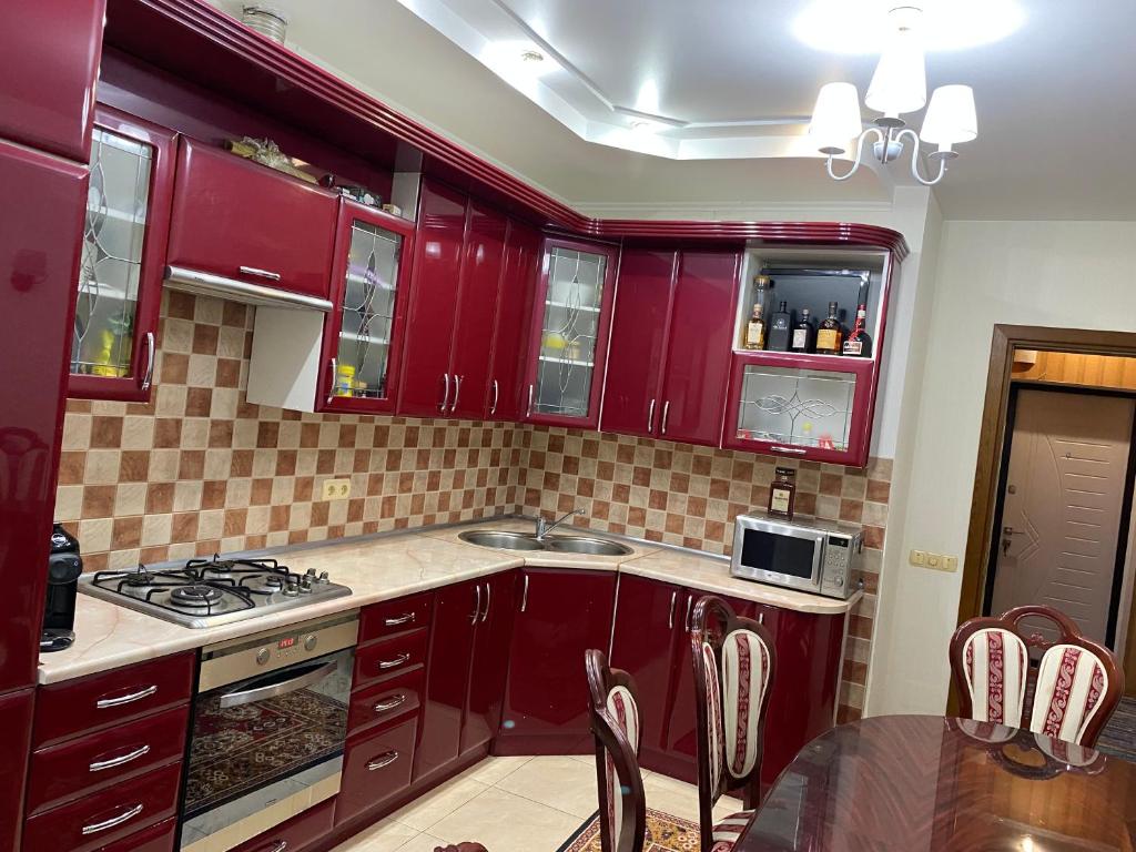kuchnia z czerwonymi szafkami, zlewem i stołem w obiekcie Apartments w Kiszyniowie