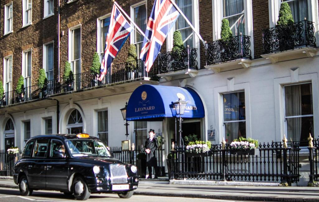 an old car driving past a building with british flags at The Leonard Hotel in London