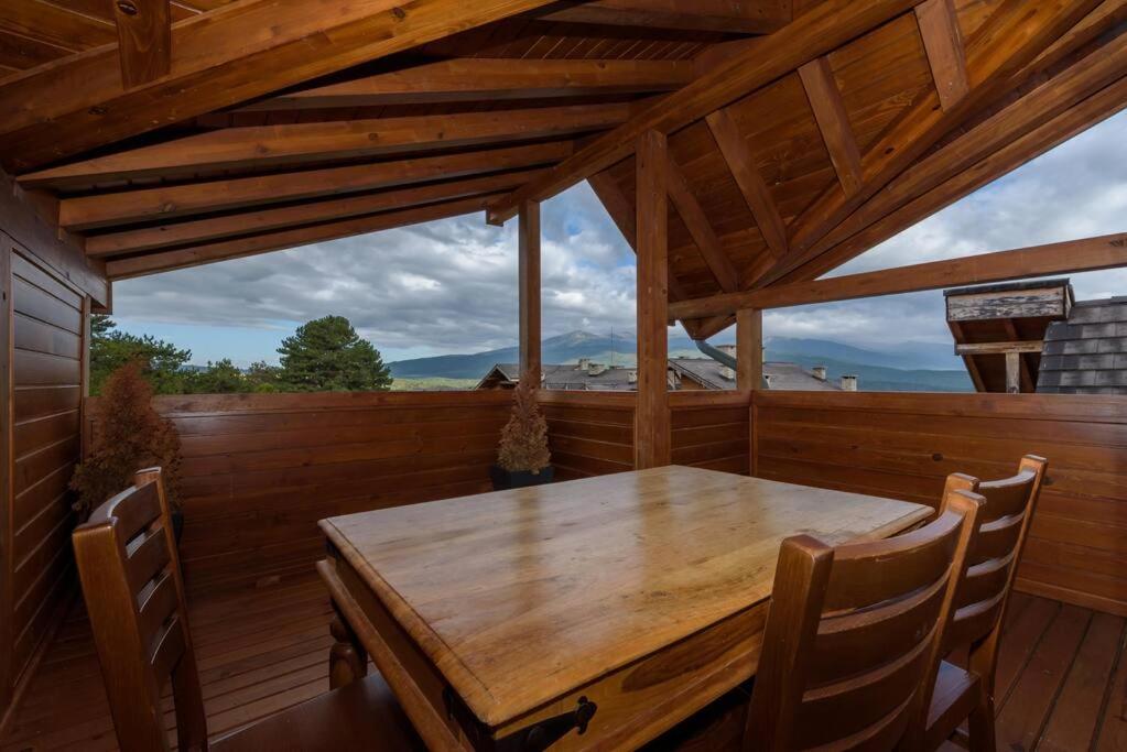 a wooden table and chairs on a porch with a wooden ceiling at Уютен апартамент с гледка в к-с Пирин Голф in Razlog