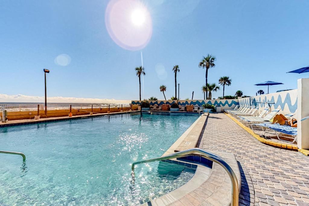 a swimming pool next to a beach with palm trees at Right Along the Beach in Daytona Beach