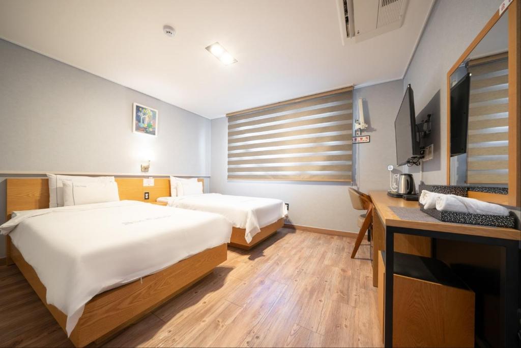 a bedroom with two beds and a desk and a television at Sea Star Hostel in Yeosu