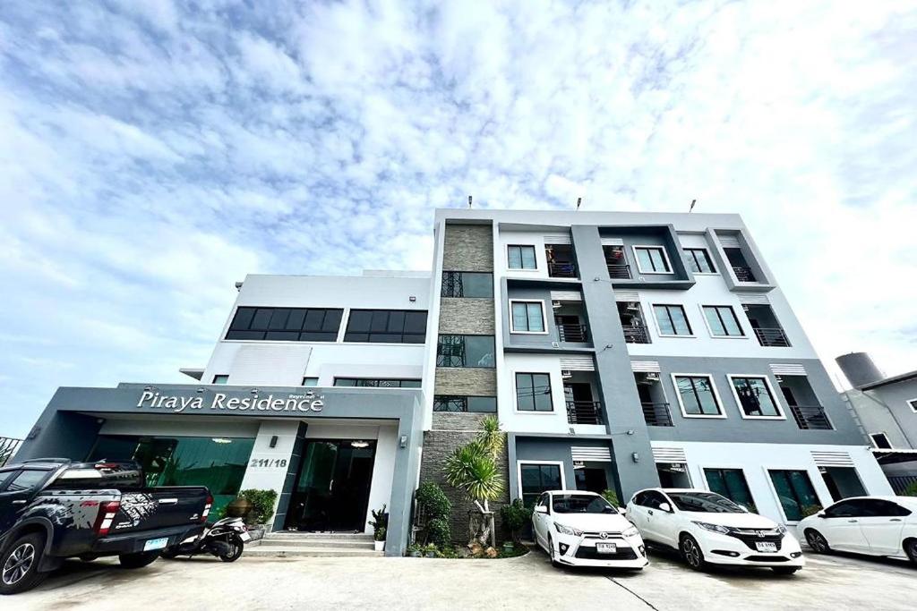 un bâtiment blanc avec des voitures garées devant lui dans l'établissement De Piraya residence, à Ban Bo Sai Klang