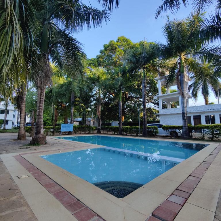 a swimming pool with palm trees in front of a building at The Majestic Royal Palms, Mtwapa in Shimo la Tewa