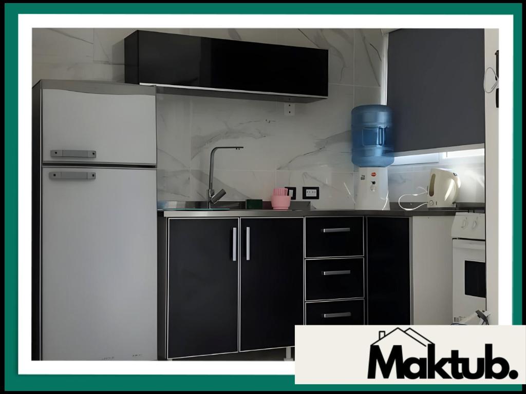 a kitchen with a white refrigerator and black cabinets at Maktub Alojamiento in San Antonio Oeste
