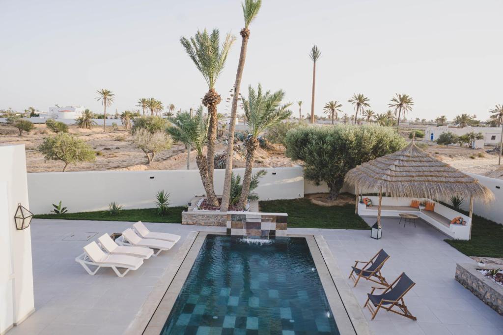 - une piscine avec des chaises, un parasol et des palmiers dans l'établissement Villa des deux oliviers Djerba, à Djerba