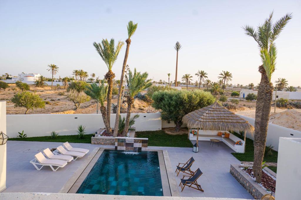 a swimming pool with chaise lounge chairs and palm trees at Villa des deux oliviers Djerba in Djerba