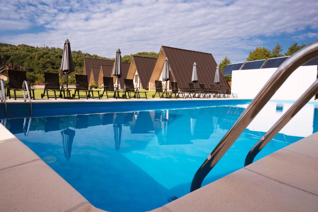 a swimming pool with chairs and umbrellas on a resort at La Casute in Căpăţîneni-Pămînteni