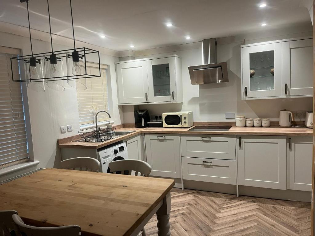 a kitchen with white cabinets and a wooden table at The cosy beach House in Llanelli