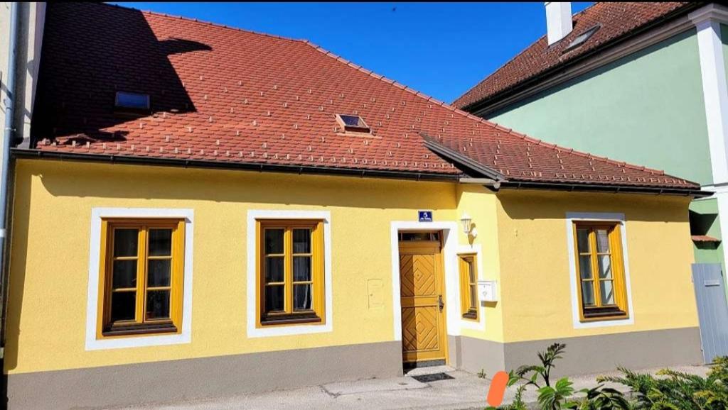 uma pequena casa amarela com um telhado vermelho em Altstadthaus Marille mit Innenhofterrasse em Melk