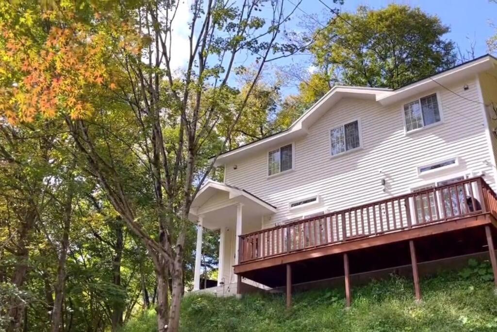 uma casa branca com um deque e árvores em 23年9月新築のレイクビューアメリカンハウス 和美インターから3分ゴルフ場近郊 em Karuizawa