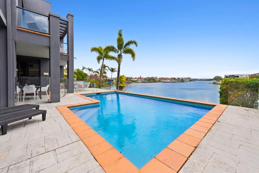 a swimming pool in front of a house with a river at Escape to Clear Island - A Palmy Waterfront Oasis in Gold Coast
