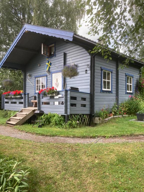 een klein blauw huis met een veranda en bloemen bij Ängsliden in Charlottenberg