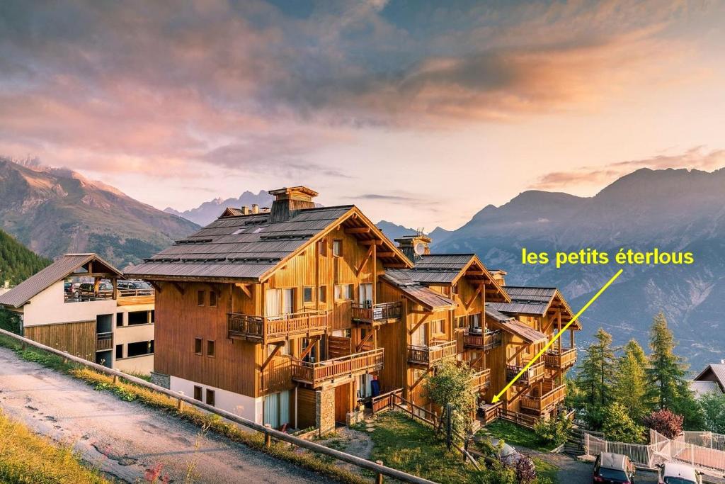 uma grande casa de madeira com montanhas ao fundo em LES PETITS ETERLOUS Appartement T3 36m2 à Puy St Vincent 1800 Alpes du sud 6 personnes parking privé couvert em Puy-Saint-Vincent