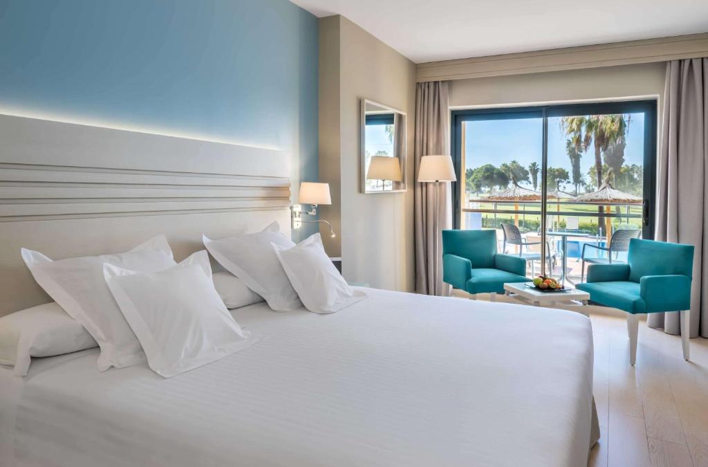 - une chambre avec un grand lit blanc et des chaises bleues dans l'établissement Barceló Costa Ballena Golf & Spa, à Costa Ballena