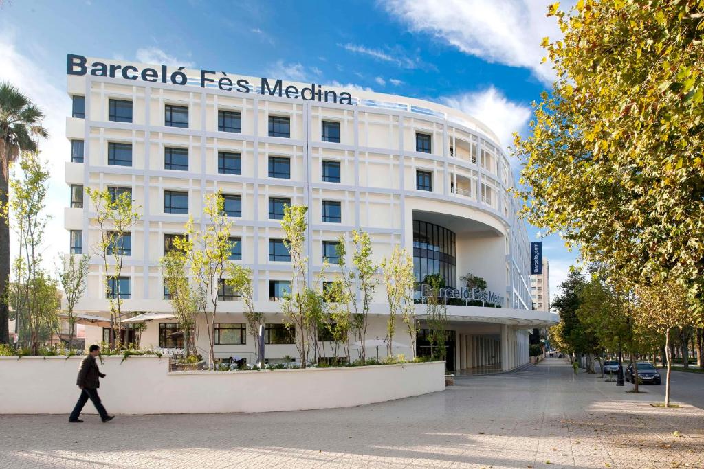 Une femme passe devant un bâtiment blanc avec un panneau. dans l'établissement Barceló Fès Medina, à Fès