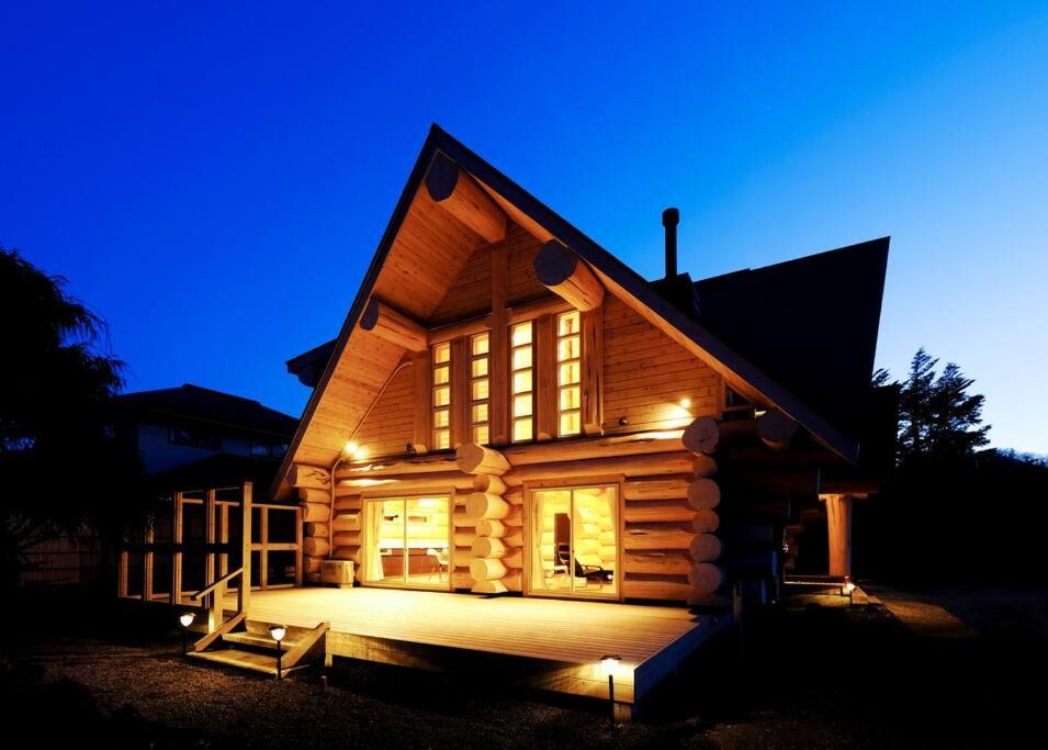 a log cabin at night with the lights on at 一度だけでも体験してほしいイエローシーダーハンドカットカナディアンログハウス in Karuizawa