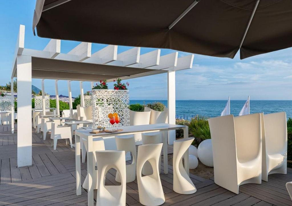 a patio with white tables and white chairs and the ocean at Hotel Oasi Di Kufra in Sabaudia
