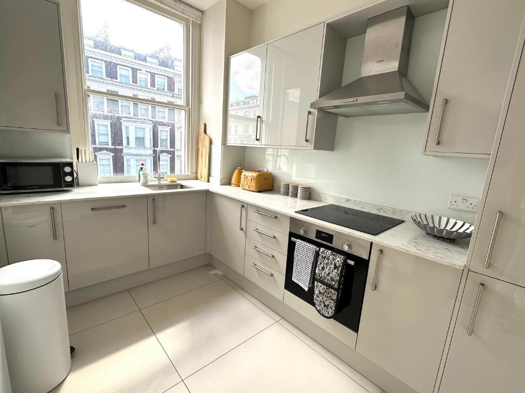 une cuisine blanche avec des placards blancs et une fenêtre dans l'établissement Cozy Flat in South Kensington, à Londres